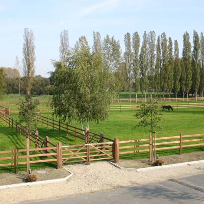 A double wooden gate gives access to a path bordered by numerous fields fenced by 3-sided wooden gates.