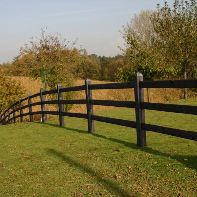 A black wooden fence with square posts and 3 rails on a field