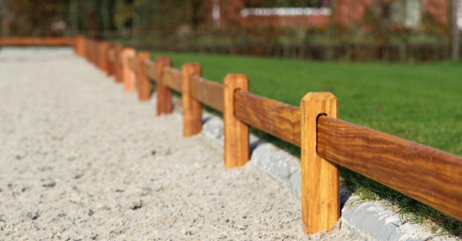 Wooden fence with square posts and a rail surrounding a dressage arena.