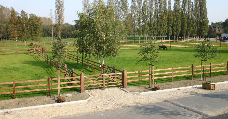 Un double portail en bois donne accès à un chemin bordé de nombreux champs clôturés par des barrières en bois de 3 lisses.