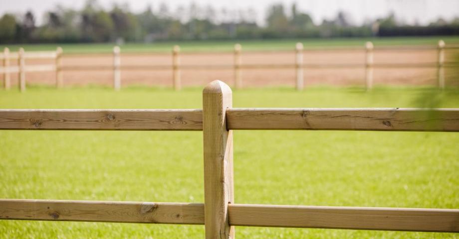 A wooden fence with two rails and square posts around a field